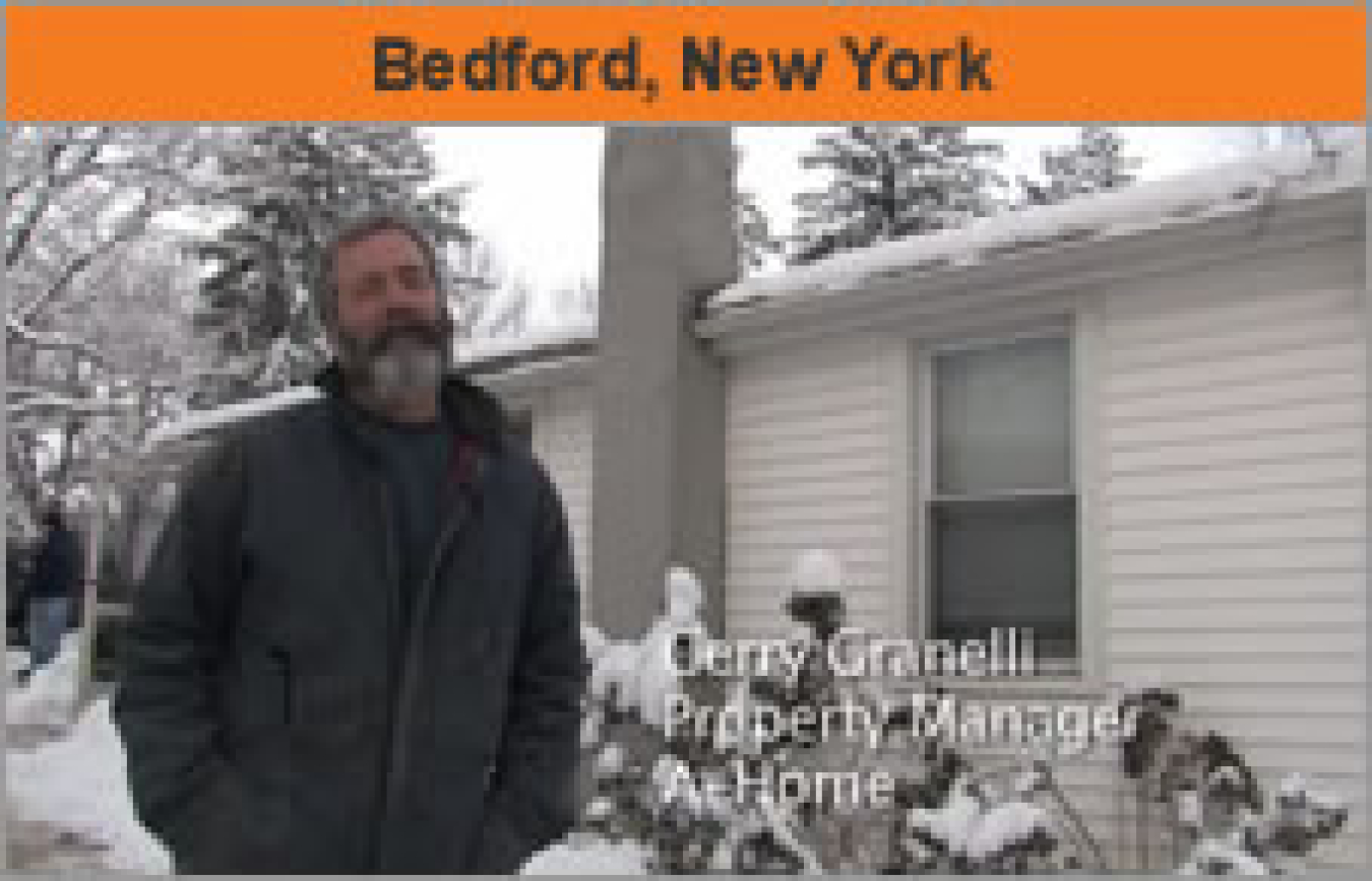 A man standing outside a house in wintertime, with the words "Bedford, New York."