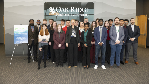 A group of people standing in front of an Oak Ridge National Laboratory sign and next to a smaller presentation sign on a stand next to them.