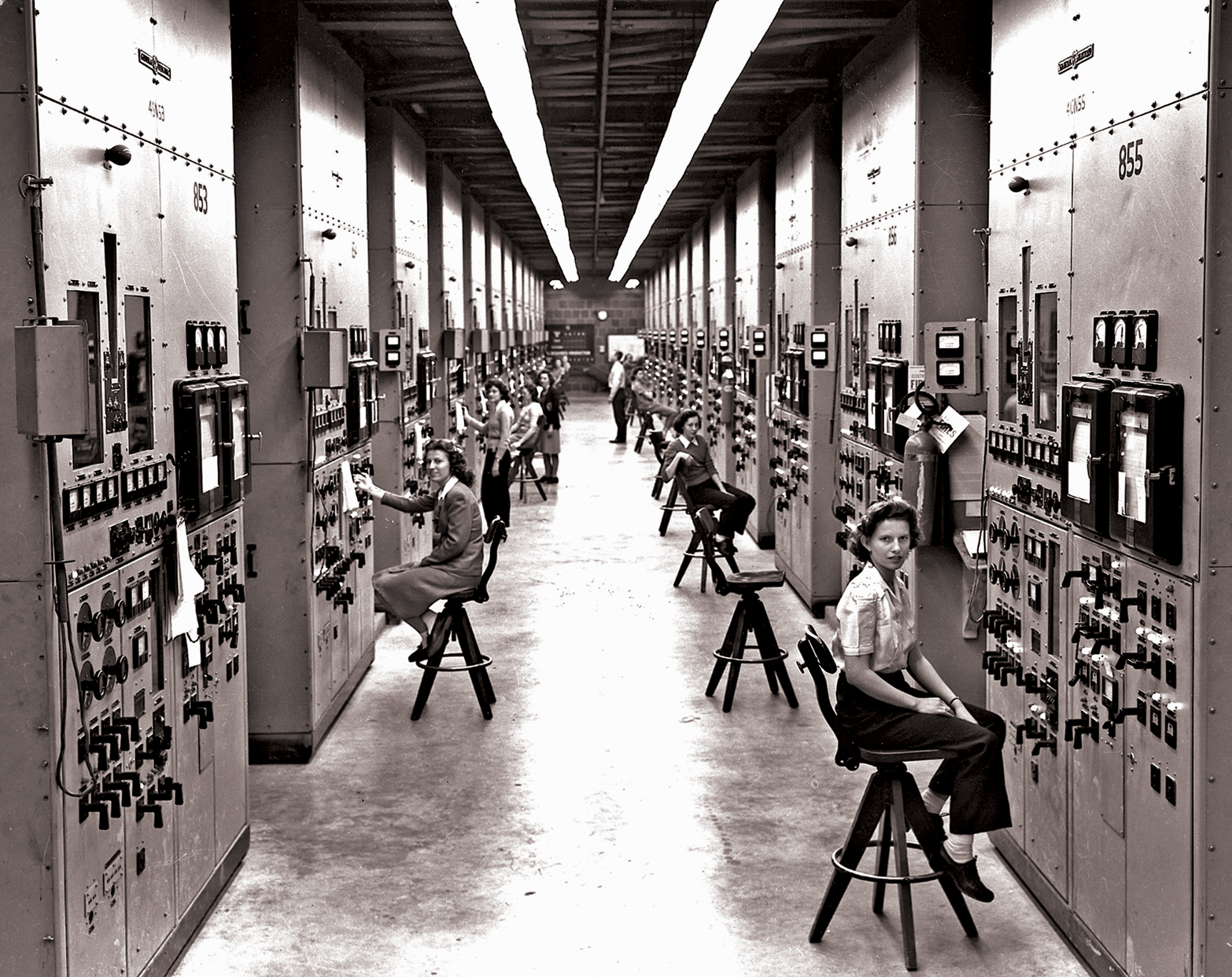 Women sit in front of industrial-sized machines in a large warehouse.